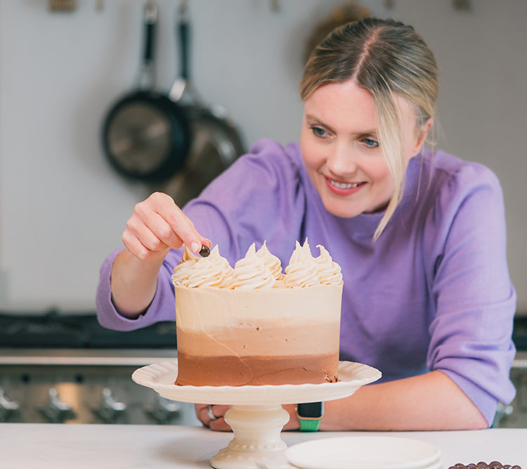 Lady decorating cake on stand in kitchen