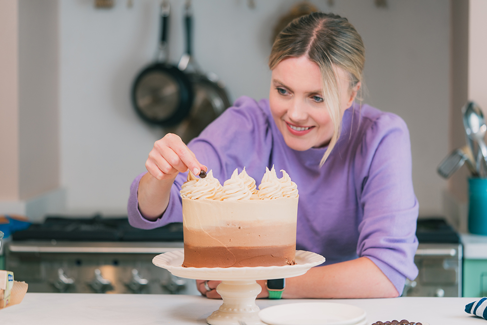 Lady decorating cake on stand in kitchen